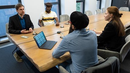 Drei Männer und eine Frau sitzen an einem Tisch in einem Besprechungsraum