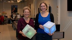 Silke Stähler-Schöpf und Berit Körbitzer stehen in ihrem Labor und halten leuchtende Würfel in den Händen