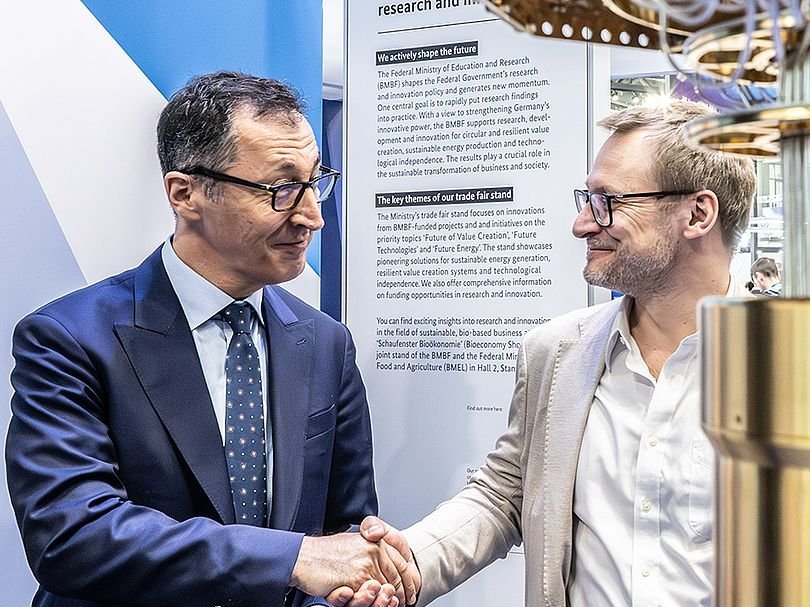 Cem Özdemir schüttelt Markus Bendele die Hand, daneben ein Kryostat eines Quntencomputers