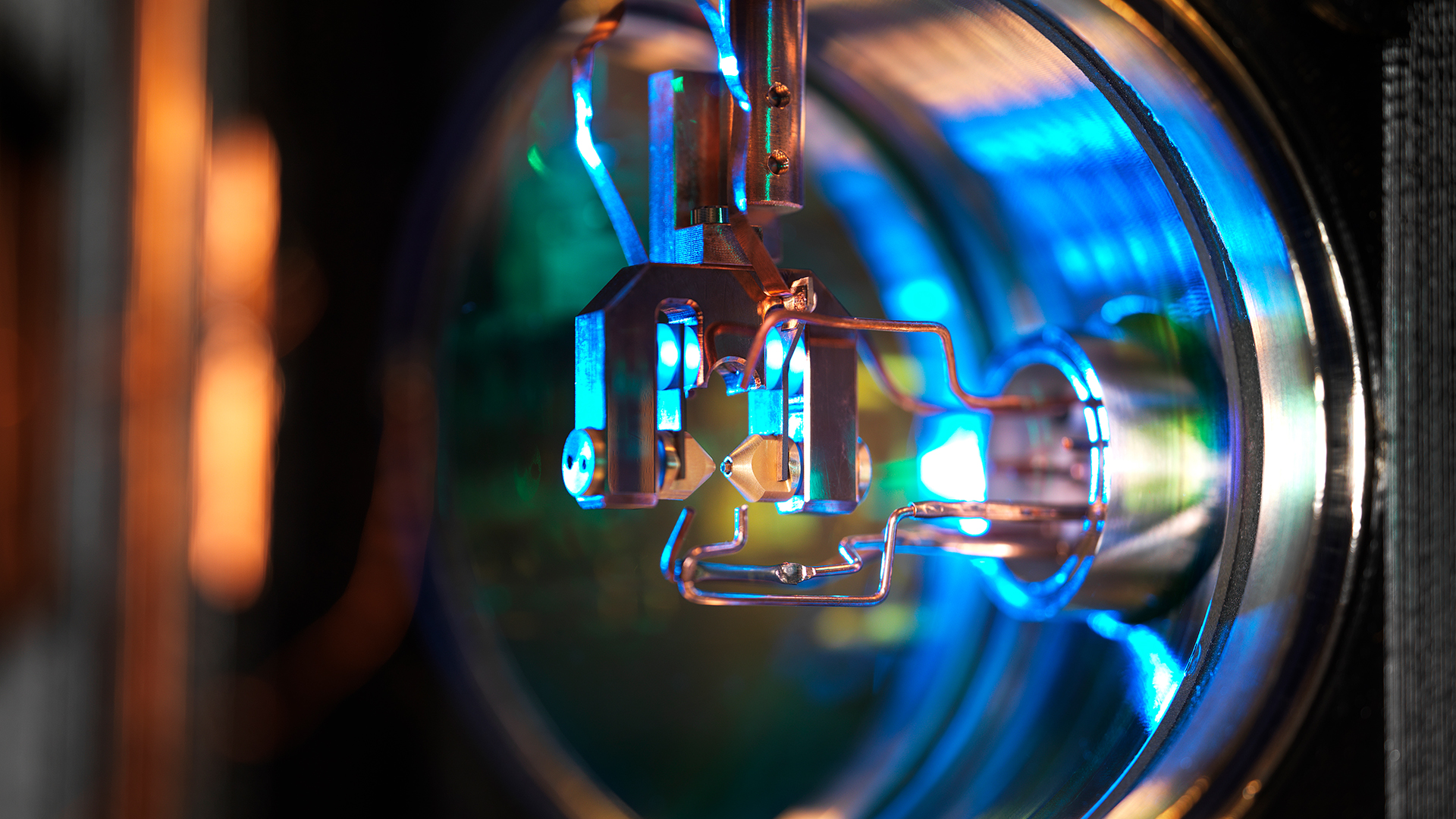 Nahaufnahme eines runden Geräts aus Metall, darin Drähte und blau-grünes Licht
